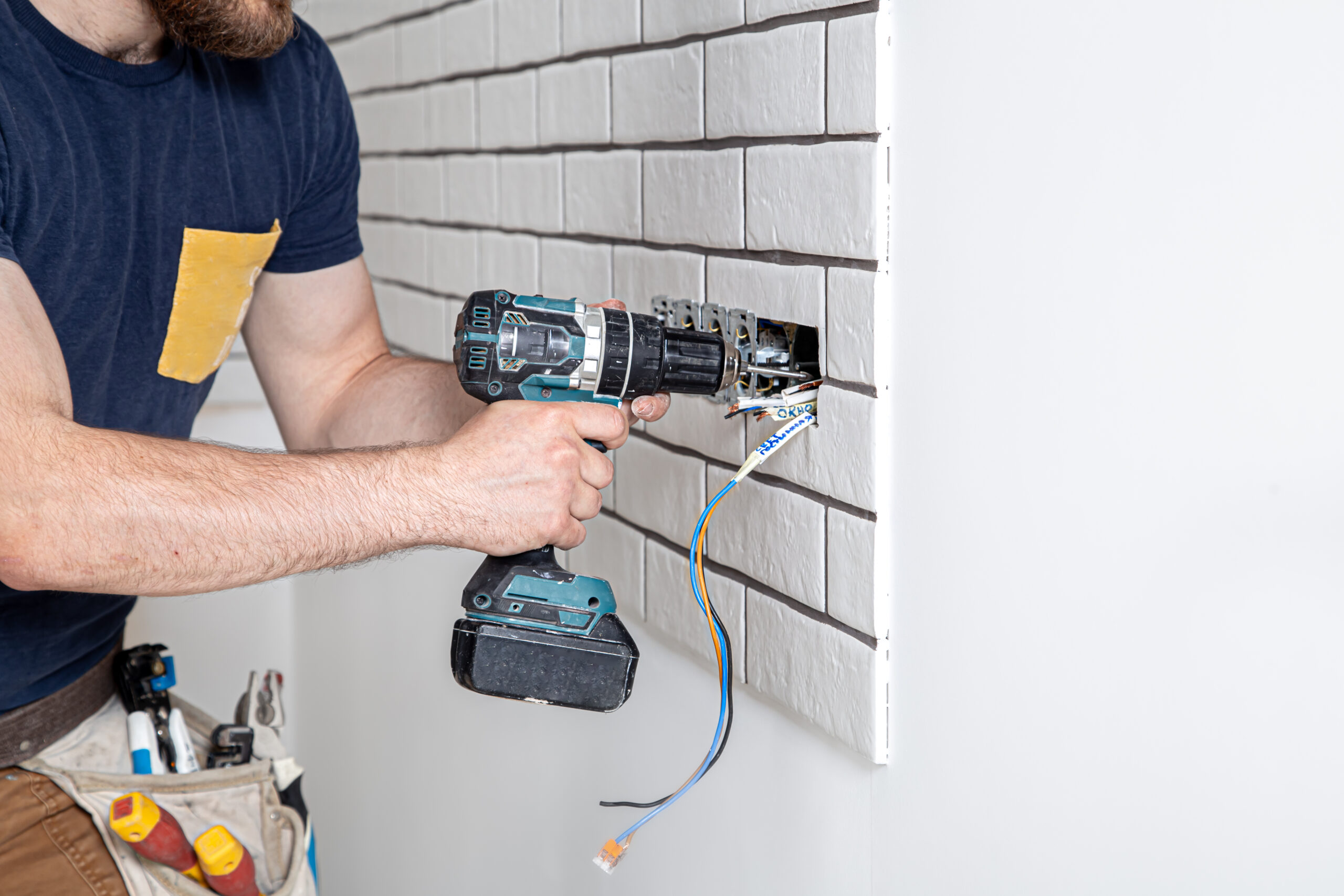 An electrician construction worker in overalls with a drill during the installation of sockets. Home renovation concept.